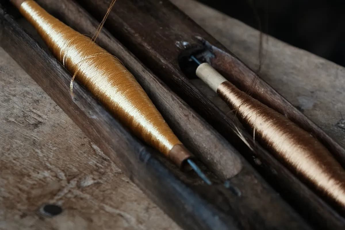 Golden Muga silk wound on bobbins beside a weaver's shuttle